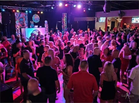 A full dance floor from behind, washed in magenta light at a TampArotic lifestyle party in Tampa Bay.
