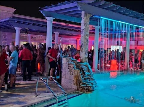 The neon-lit pool and cabana at a TampArotic hotel-takeover pool party in Tampa Bay, with guests gathered around the glowing water.